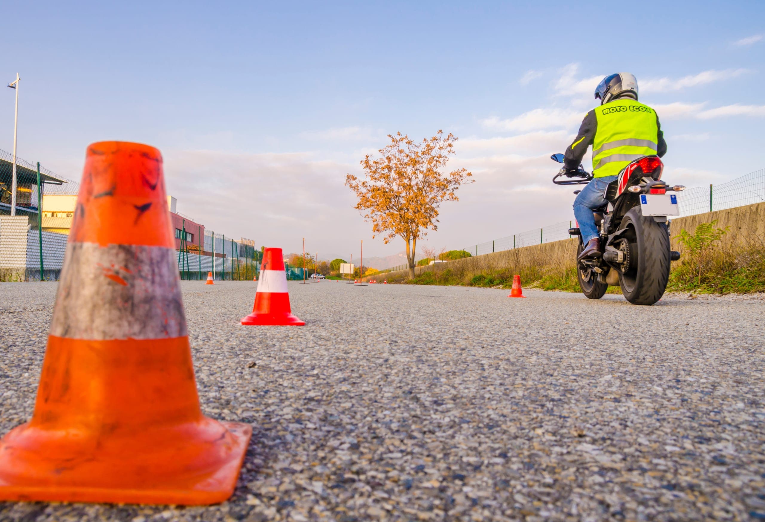 Élève en gilet jaune sur une moto, sur un plateau d'entraînement balisé de plots